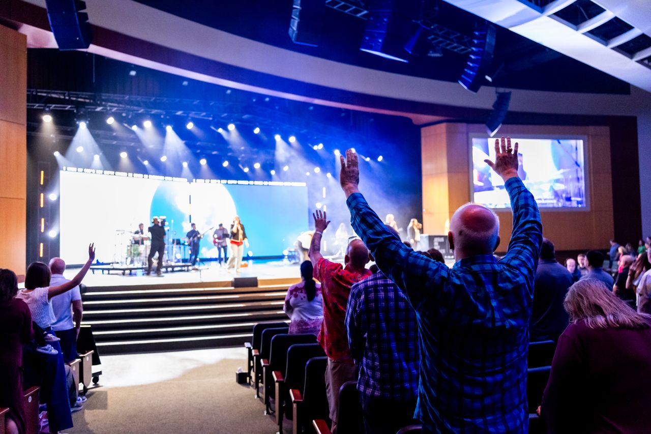 A lively worship service with an audience raising hands to a live band on stage in a church.